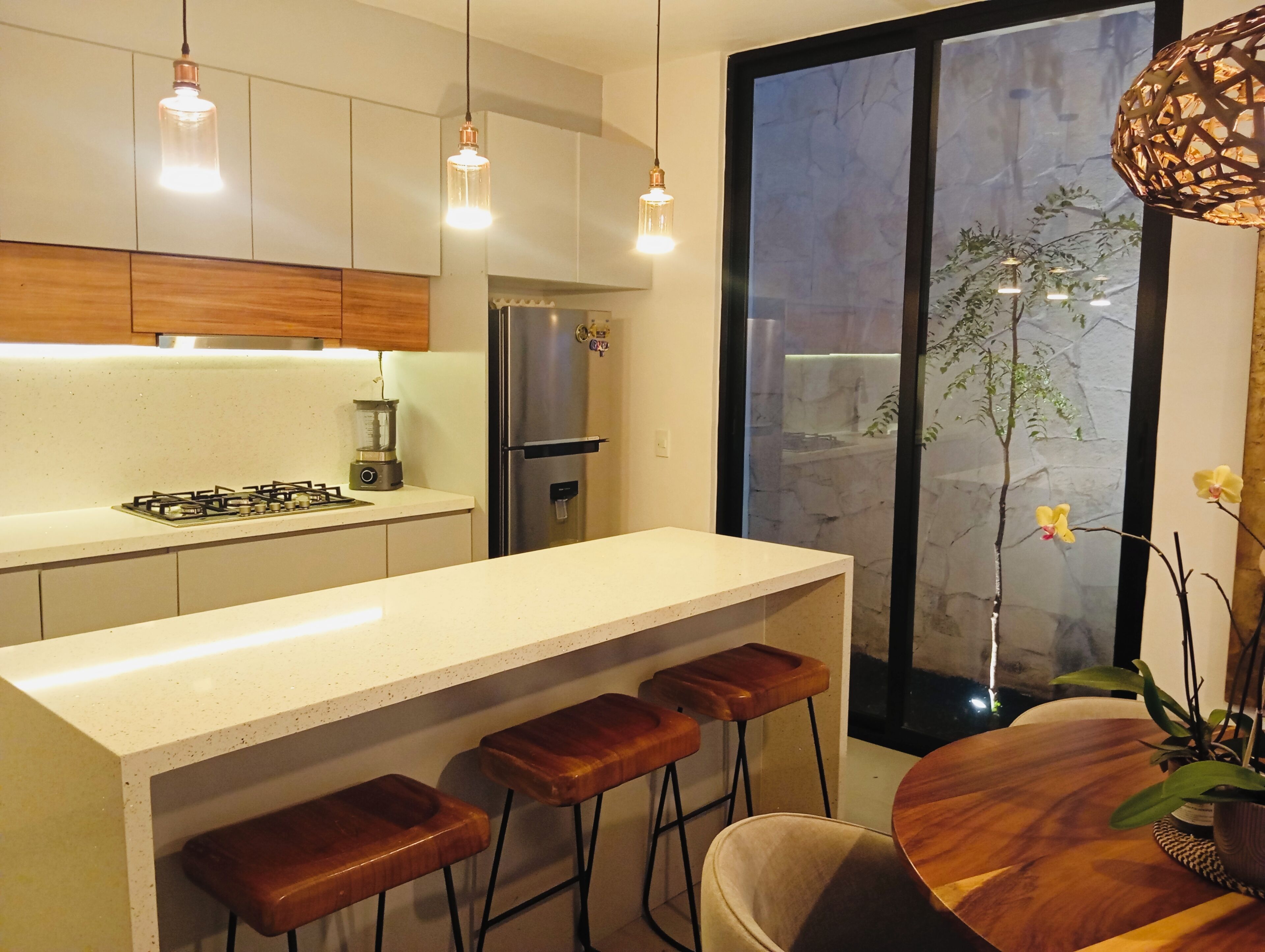 A modern kitchen with a central island, bar stools, stainless steel appliances, and pendant lighting.