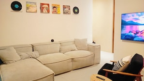 A living room with a sectional sofa, a small wooden table, a black chair, and a flat-screen TV.
