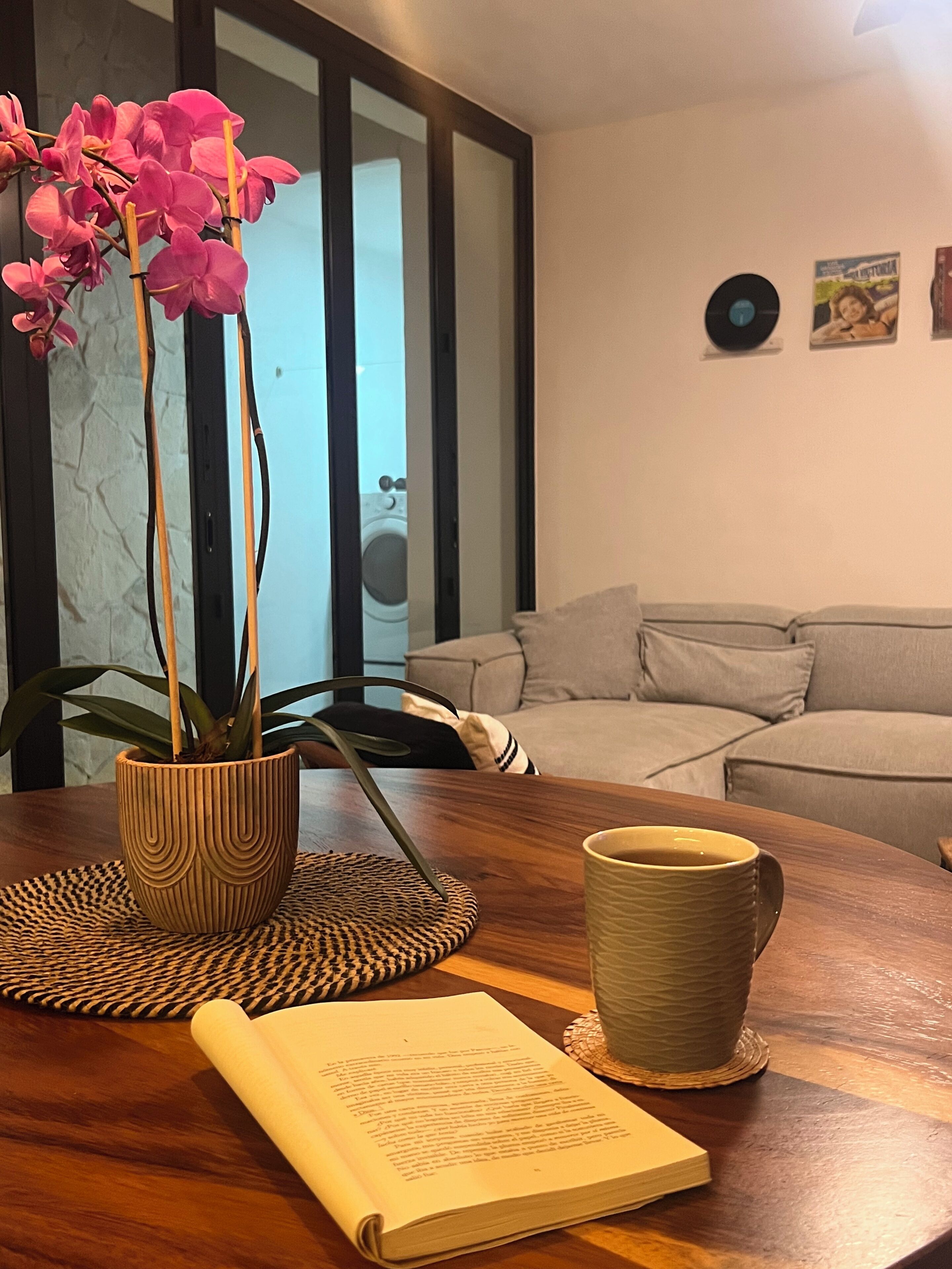 A wooden table with a potted orchid, a mug, and an open book.