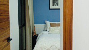 A bedroom with a bed, a nightstand, a framed picture on the wall, and a window with curtains.
