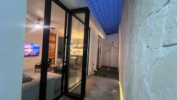An interior space with a glass door leading to a dining area, a television mounted on the wall, and a ceiling with a grid pattern.