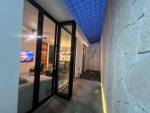 An interior space with a glass door leading to a dining area, a television mounted on the wall, and a ceiling with a grid pattern.
