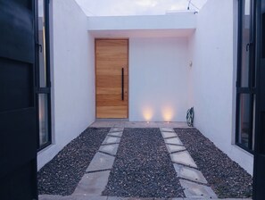 A modern entrance with a wooden door, a gravel pathway, and a hose on the right.