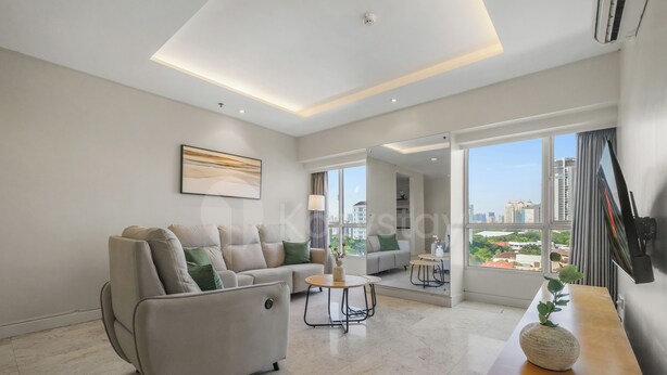 A modern living room with a sofa, a coffee table, and a view of the city through large windows. - Solea by Kozystay - Senayan (South Jakarta)