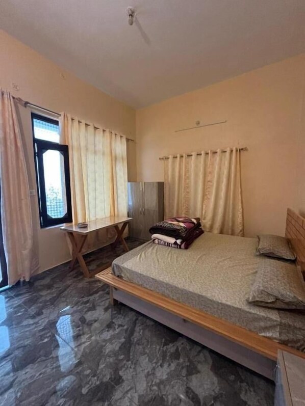 A bedroom with a bed, a desk, and a window with curtains.