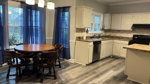 A kitchen with a dining table, chairs, a dishwasher, cabinets, and a stove.