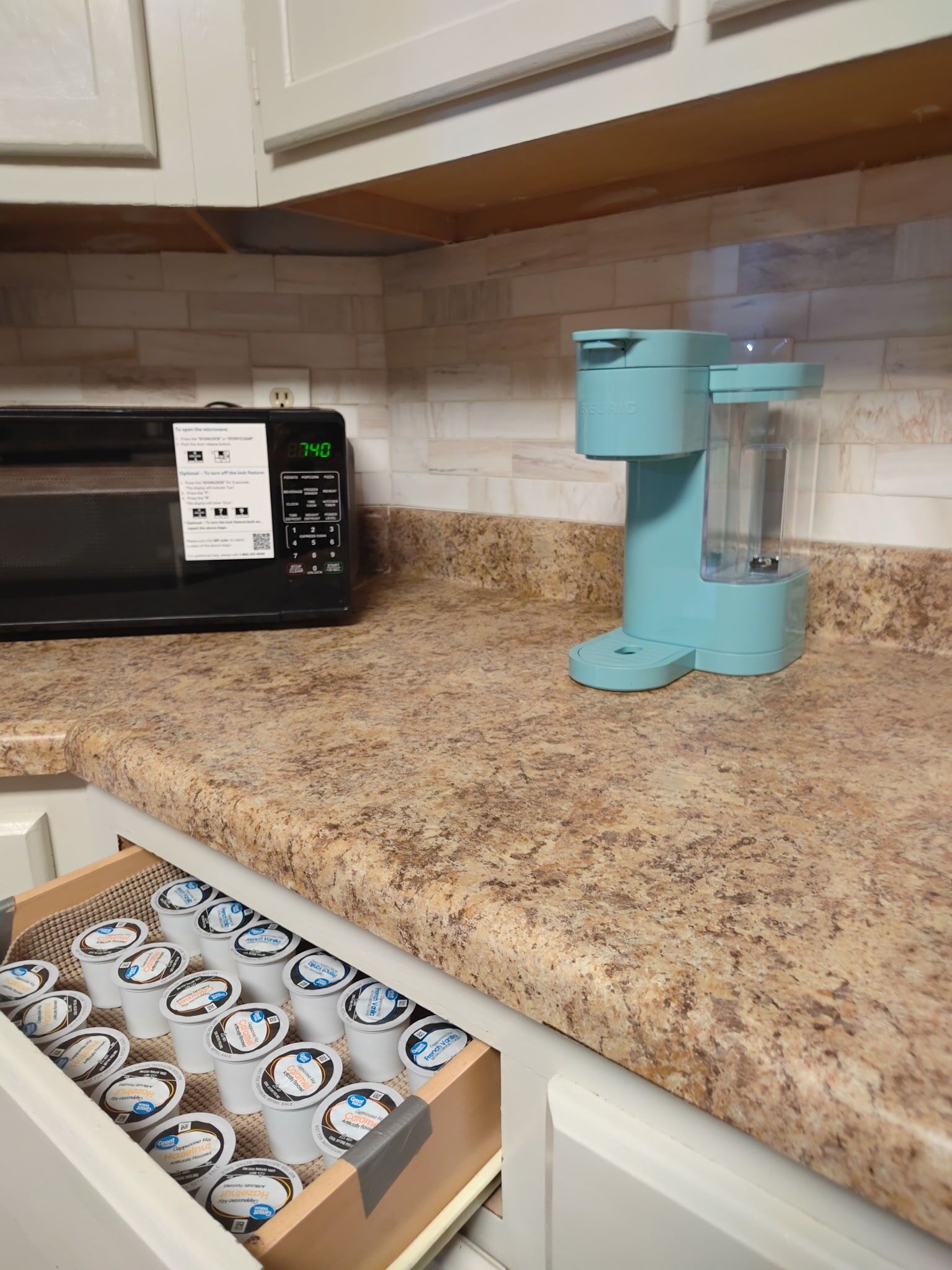 A kitchen with a microwave, a coffee machine, and a drawer with yogurt containers.