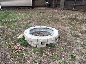 Ein Steine Feuerkorb in einem Garten mit Gras und herabgefallenen Blättern.