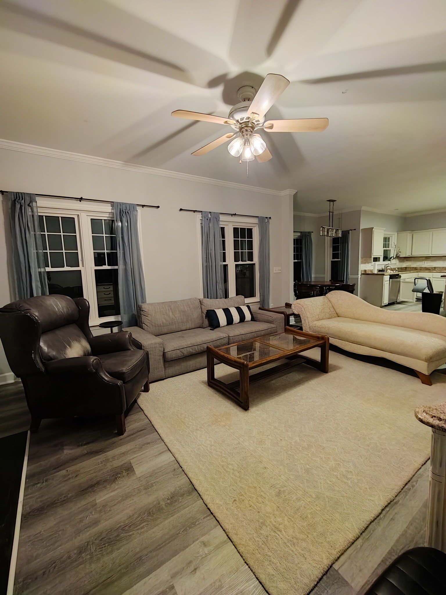 A living room with a ceiling fan, a sofa, a coffee table, and a dining area in the background.