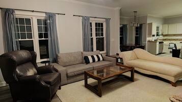A living room with a ceiling fan, a sofa, a coffee table, and a dining area in the background.