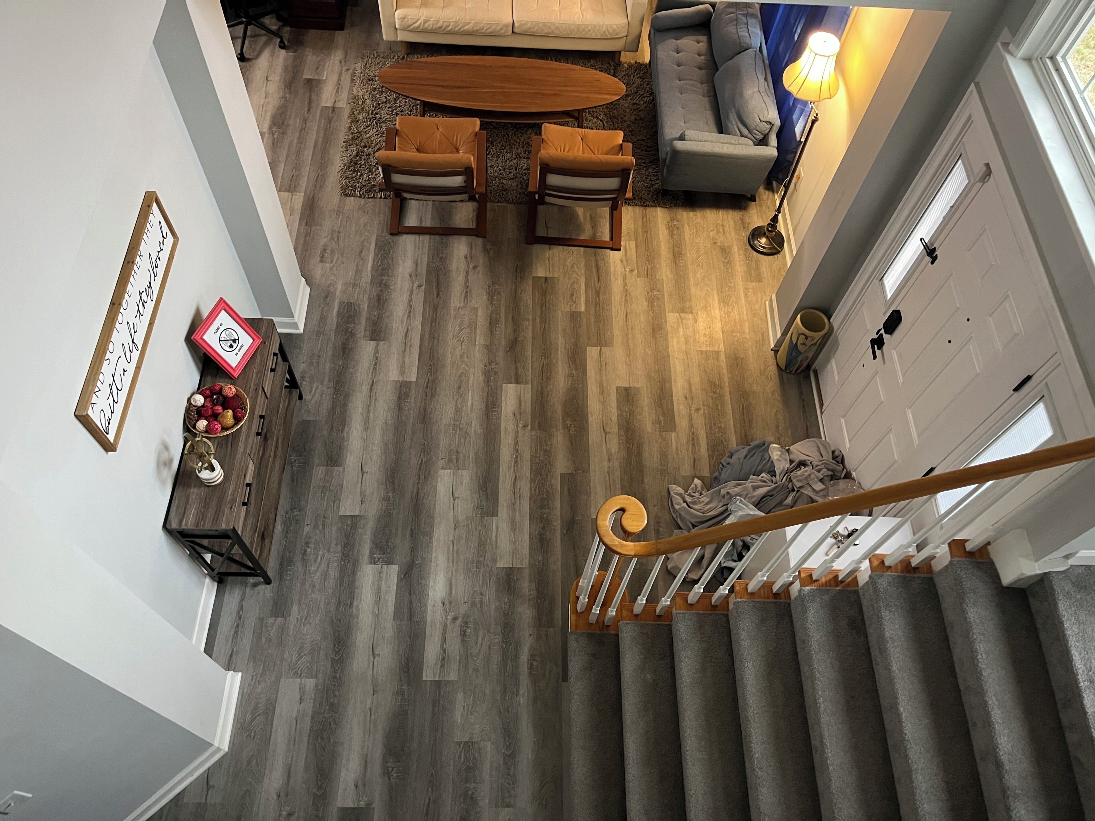 A spacious living area with a sofa, coffee table, and chairs, a staircase with a railing, and a wooden floor.