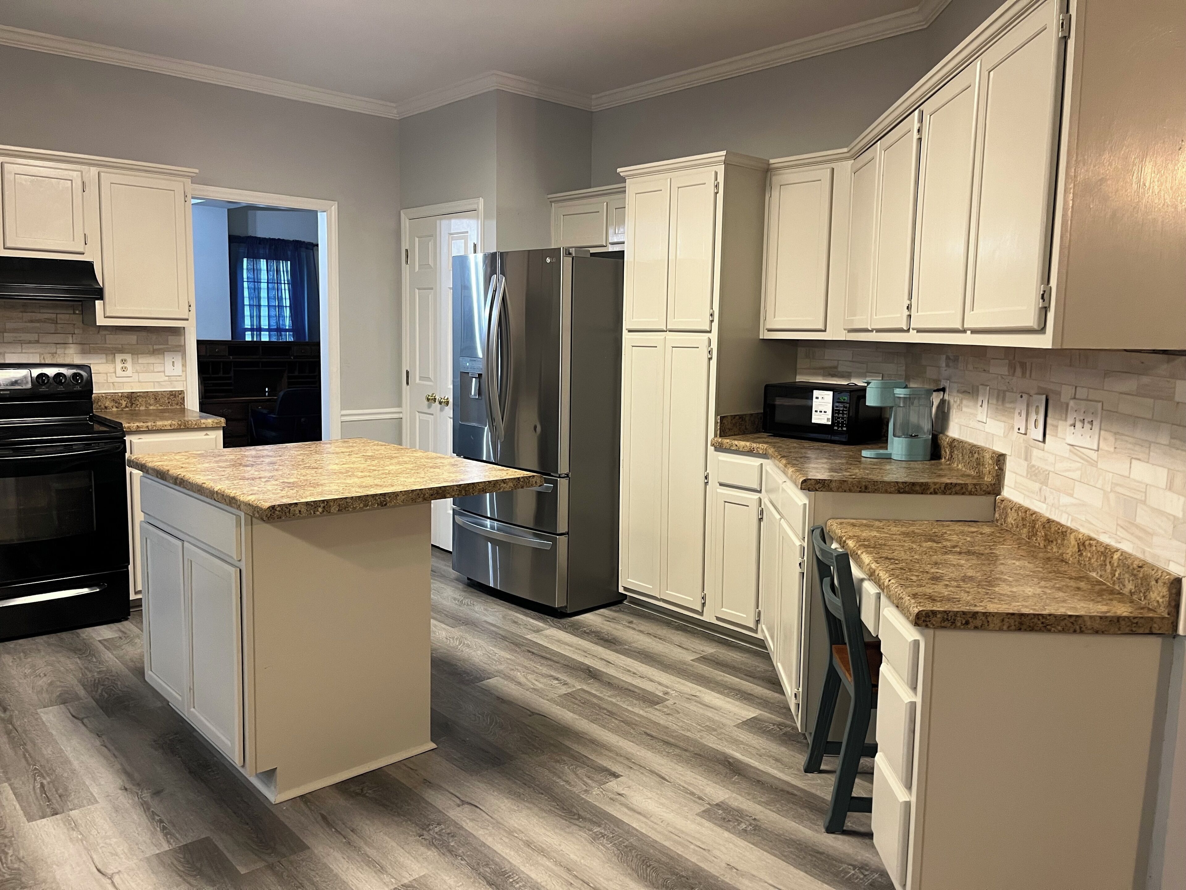 A modern kitchen with a central island, stainless steel appliances, and light-colored cabinetry.