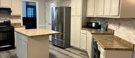 A modern kitchen with a central island, stainless steel appliances, and light-colored cabinetry.