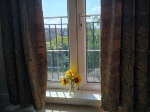 Ein Fenster mit Blick auf eine Wohngegend, Vorhänge und eine Vase mit Sonnenblumen.