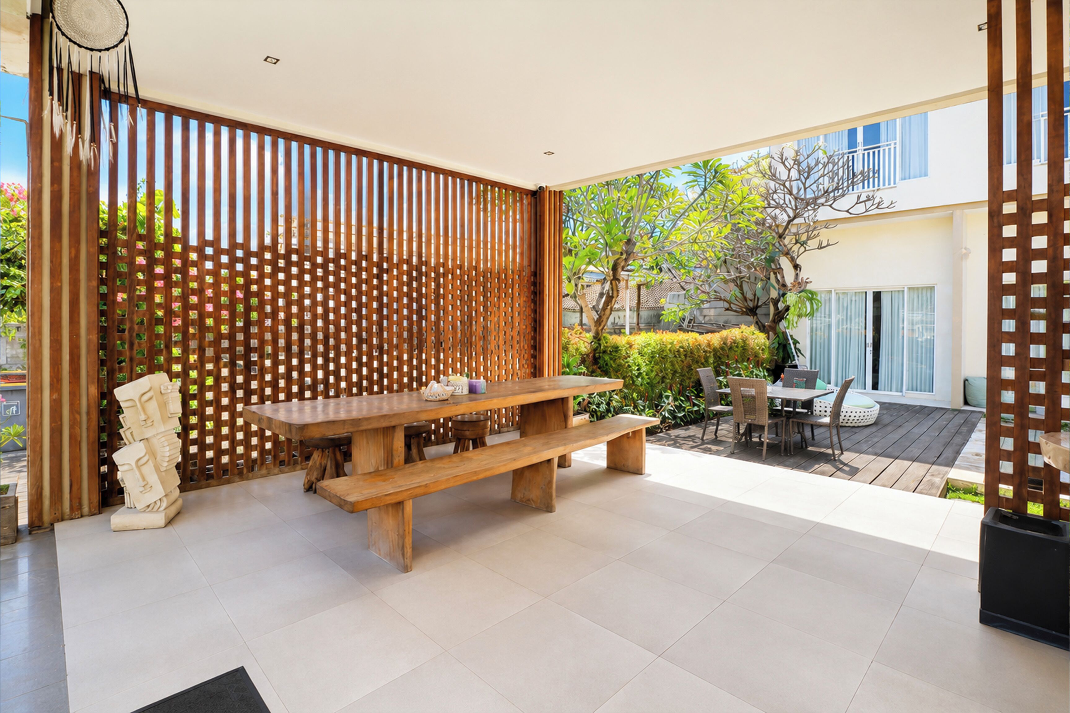 Un área de comedor exterior moderna con una mesa y bancos de madera, rodeada por una valla de madera y vista a un edificio.