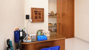 Una recepción con una silla azul, un mostrador de madera, un aire acondicionado instalado en la pared, un panel de madera decorativo y una pequeña estatua.