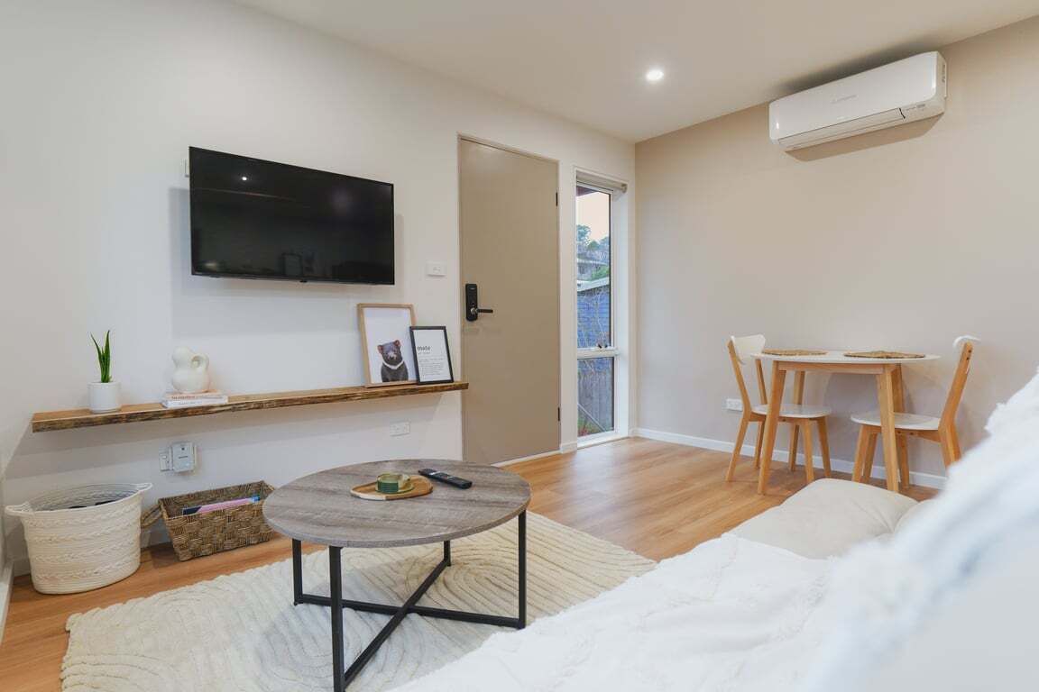 A modern living room with a flat-screen TV, a round coffee table, a sofa, a dining area with a table and chairs, and an air conditioning unit.