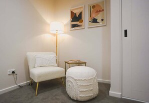 Una habitación con un sofá blanco, un otoman redondo, una lámpara de pie y dos cuadros abstractos en la pared.