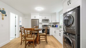 Cozinha moderna com armários brancos, eletrodomésticos de aço inoxidável e um espaço de refeições com cadeiras de madeira.