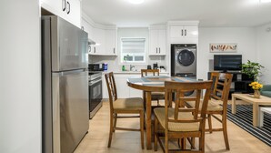 Uma cozinha moderna com eletrodomésticos de aço inoxidável, uma área de refeições com cadeiras de madeira e uma TV de tela plana.