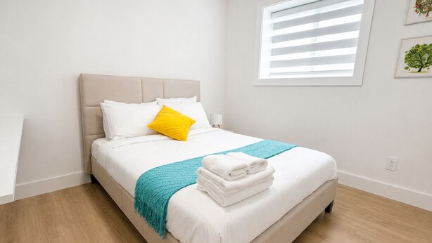 Cama bem arrumada com lençóis brancos, cabeceira bege e manta azul-turquesa.
