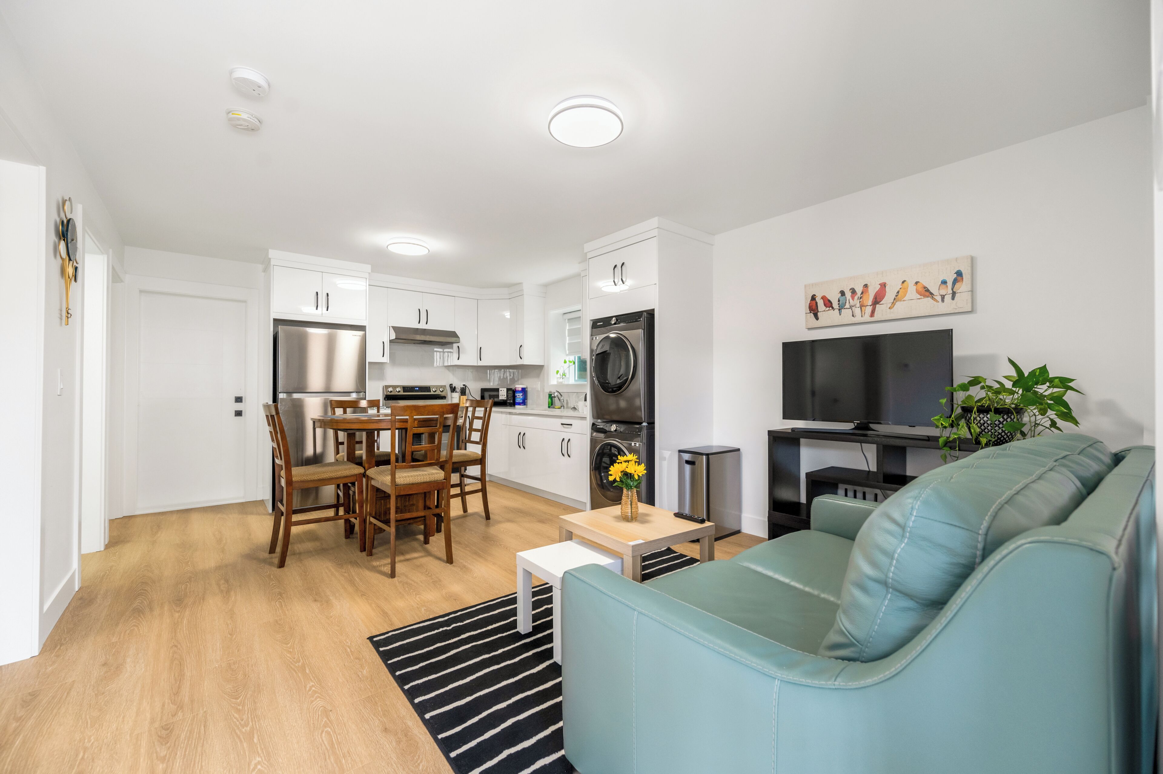 A modern apartment with a dining area, kitchenette, and a living room with a sofa and TV.