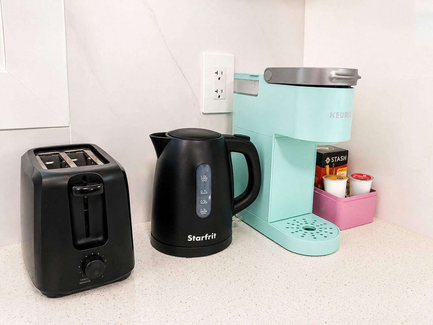 A kitchen with a toaster, a coffee maker, and a pink container with coffee pods.