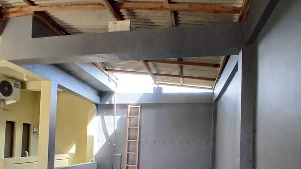 Une pièce avec un sol en béton, une échelle appuyée contre le mur et une porte avec une fenêtre.