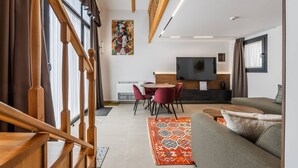 Una sala de estar moderna con una escalera de madera, un comedor con sillas rojas, un televisor grande y un sofá.
