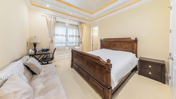 A bedroom with a large bed, a bedside table, a nightstand, a sofa, and a window with curtains.