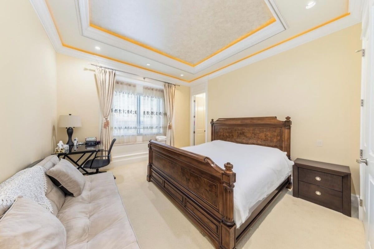 A bedroom with a large bed, bedside tables, a desk with a chair, and a window with curtains.