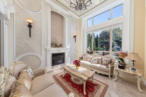 Un salón lujoso con chimenea, muebles elegantes y un amplio ventanal con vistas al exterior.