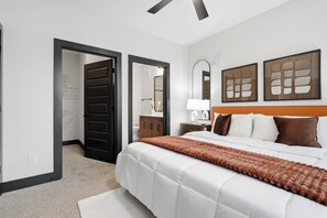 A hotel room with a large bed, a wooden headboard, a nightstand with a lamp, and a mirror on the wall.