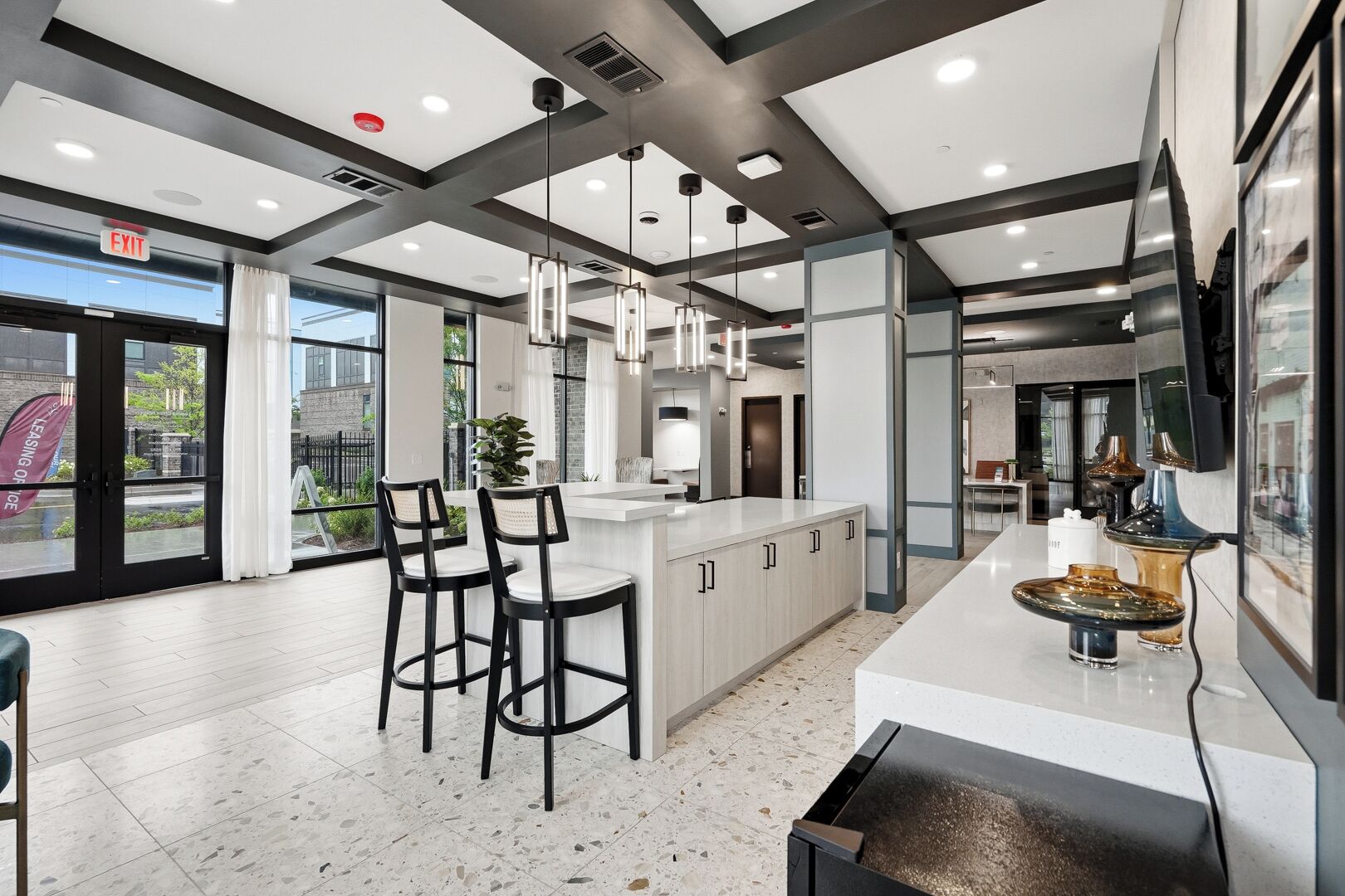 A modern kitchen with a central island, bar stools, pendant lighting, and a large window providing natural light.