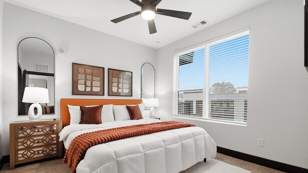 A bedroom with a bed, a nightstand, a ceiling fan, a window with blinds, and wall art.