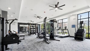 A modern gym with ceiling fans, various exercise equipment, and large windows.