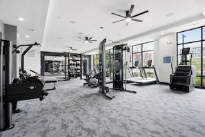 A modern gym with ceiling fans, various exercise equipment, and large windows.