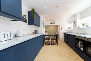 A modern kitchen with dark blue cabinets, a marble countertop, a built-in oven, and a dining area with a bench.