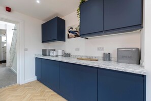 A modern kitchen with dark blue cabinets, a marble countertop, and a bread maker.
