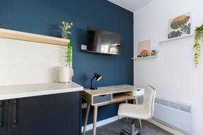Ein modernes Zimmer mit Schreibtisch, Stuhl, Fernseher und Zierpflanzen.