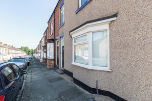 A row of terraced houses with a narrow street, parked cars, and a clear sky.