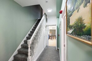 A staircase with carpeted steps and white balusters, leading to a room with a painting on the wall. - 6BR 6 Bath | Workspace | Family & Contractors (Darlington)