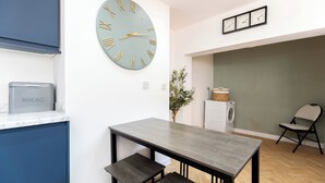 Ett modernt kök med en stor väggklocka, ett matbord med bänkar, en tvättmaskin och en liten växt.