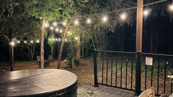 A covered outdoor deck with a hot tub, wooden benches, and string lights.