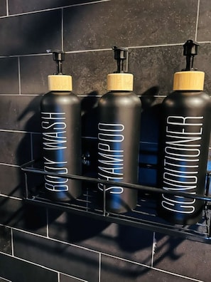 Trois bouteilles noires, étiquetées, sont disposées sur une étagère contre un mur carrelé.