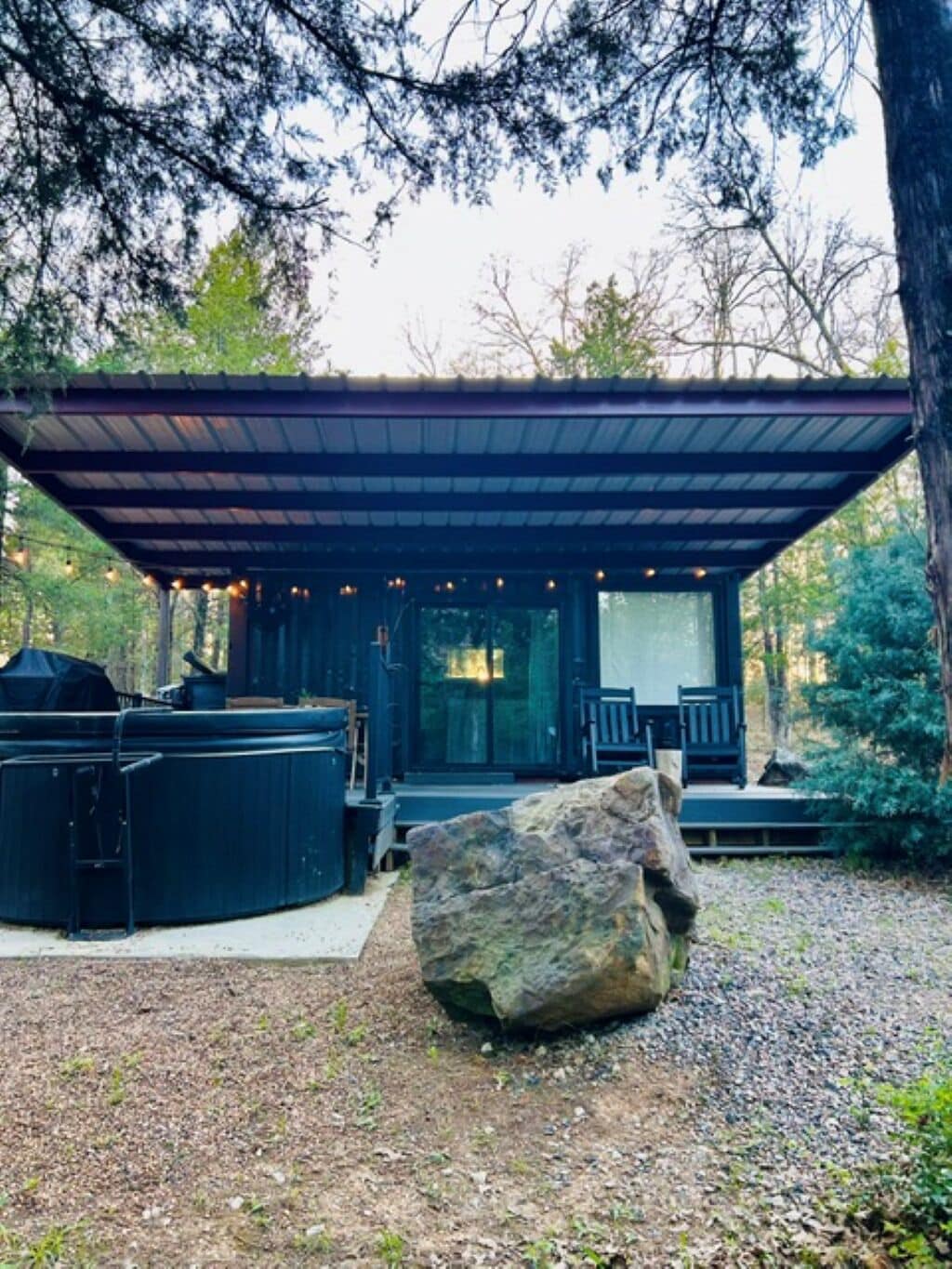 Un espacio de estar al aire libre techado, con una parrilla, una gran roca y vistas de los árboles circundantes.