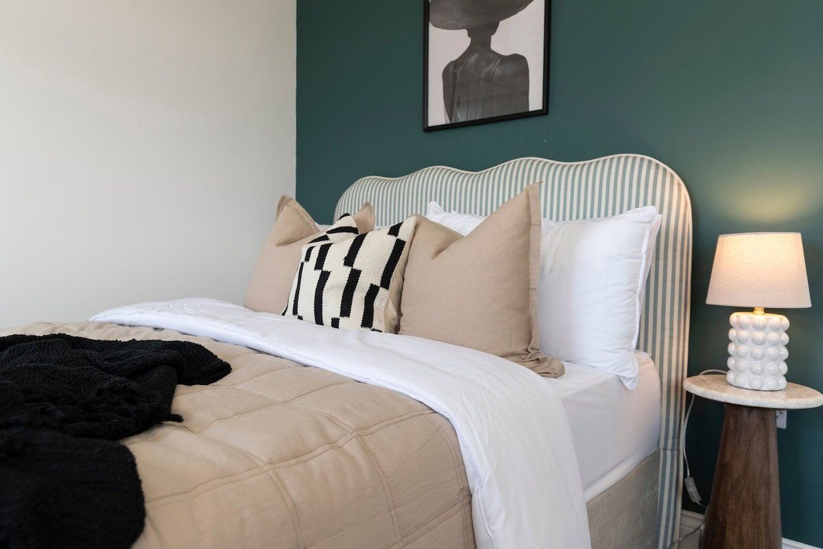 A bed with a striped headboard, multiple pillows, a black throw blanket, and a bedside lamp.