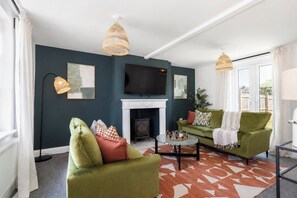 A living room with a fireplace, green sofas, a television, and a patterned rug. - Durham 3BR -Parking free- Contractor friendly (Meadowfield)