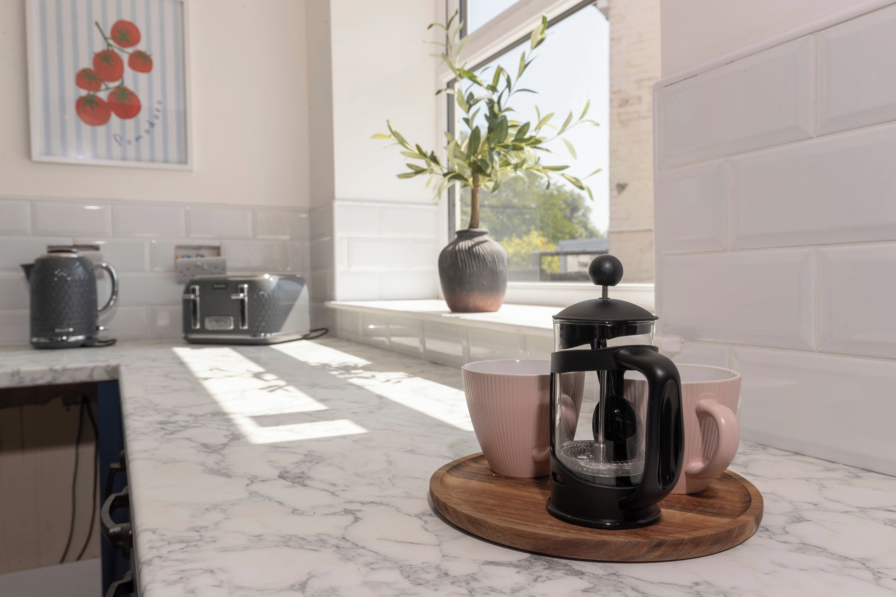 Una cocina con cafetera sobre una tabla de madera, un tostador y una tetera en la encimera.
