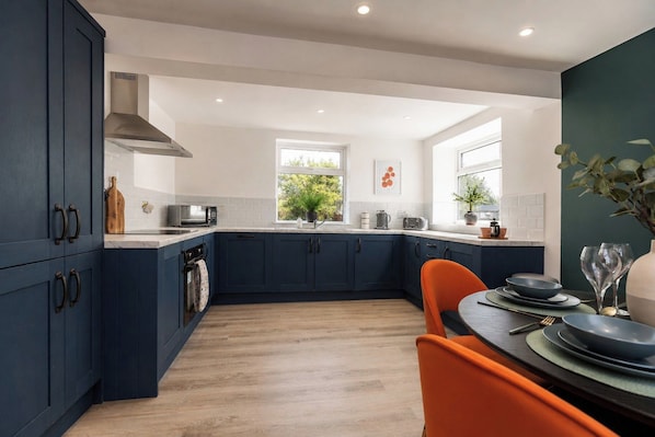 A modern kitchen with dark blue cabinets, a wooden countertop, and a dining area with a table set for two. - Stylish 3BR Durham Home | Contractors & Families (Meadowfield)
